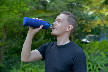 A man drinks water from a sports bottle after jogging in the park. Tired exhausted and thirsty...