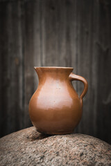 Clay jug on the rock with wooden background. Vintage styles.

Close-up of old container on table.
