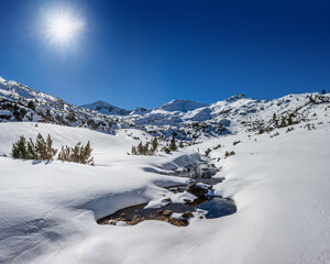 Bunderishka river under the snow and mountains on the horizon in sunny winter morning. Pirin...
