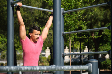 Fototapeta premium Young athlete is strengthening his core muscles by performing hanging leg raises on an outdoor gym