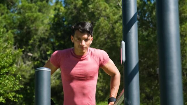 Athletic man doing tricep dips on outdoor parallel bars in a park, focusing on upper body workout under bright sunlight