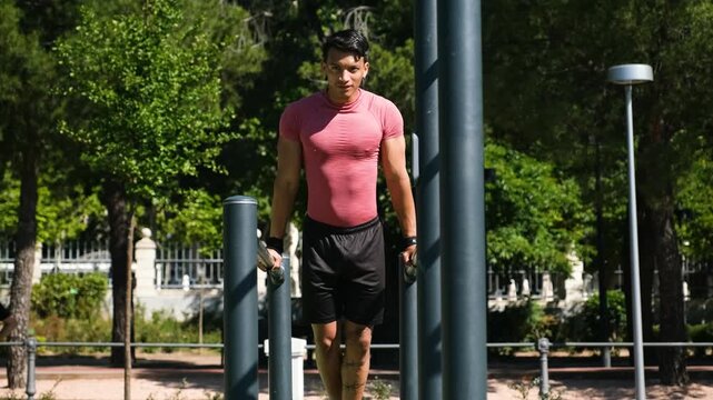 Athlete exercising on parallel bars in a park, performing dips with controlled movements on a sunny day