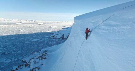 Man digging snow with shovel on glacier in Antarctica. Winter wild nature aerial panorama. People enjoy sunny day on Antarctic iceberg slope hill. Discover South Pole, travel, expedition, exploration.