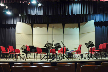 Empty concert stage with red chairs, music stands, and instruments ready. © Marquicio