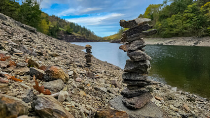 Sculptures of towers of stones on shore of beautiful lake, with blue sky, rocks and trees on lake...