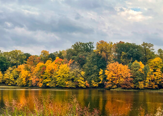 View of a treelined shoreline of a lake in autumn reflected in the water