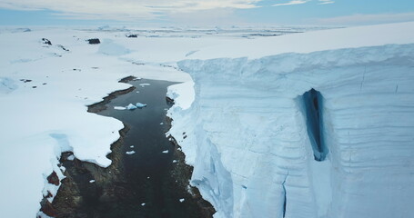 Towering glacier over ocean bay canyon in Antarctica. Winter landscape wild nature. Iceberg giant ice wall above rocky coast. Polar environment. Ecology, melting ice, climate change, global warming