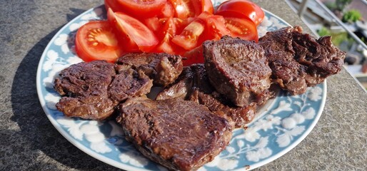 Dinner with steak and tomatoes in a plate with blue decoration