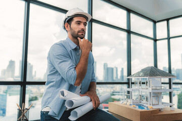 Portrait of professional architect engineer thinking about modern house project while wearing safety helmet and casual outfit. Smart interior designer holding project plans near house model. Tracery.