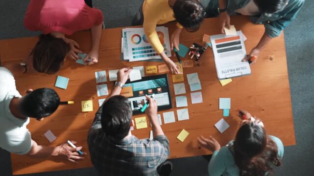 Top view of business people working together to design web design. Aerial view of designer brainstorming and discussing about website interface and looking at tablet with digital design. Symposium.