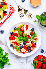 Fruit summer salad with berries, ricotta cheese, mint and honey, white marble background, top view