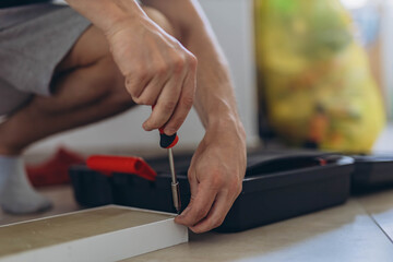  Close-up of a man's hands screwing screws into a wooden shelf on the floor using a screwdriver