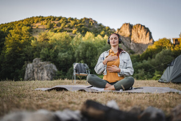 Fototapeta premium Young woman with headphones have guided meditation on the mountain