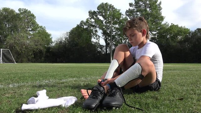 Low angle shot of a little boy soccer player having difficulty putting on his shin guards before a game