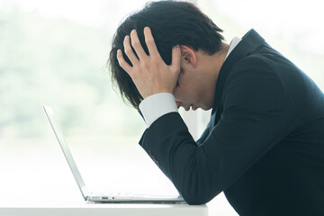 デスクで頭を抱えながら悩む若い男性ビジネスマン
