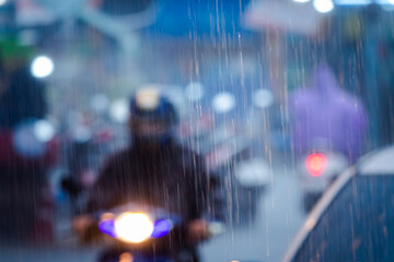 Fototapeta premium A blurry image of a rainy street with a man on a motorcycle and a woman in a purple jacket