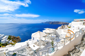 Fototapeta premium Whitewashed luxury resorts with sidewalk cafe terraces above the blue sea and caldera at the hillside town of Oia, on the island of Santorini, Greece.
