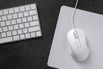 Wired mouse with mousepad and computer keyboard on dark textured table, flat lay