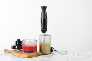 Hand blender kit and mixtures of ingredients on white marble table, space for text