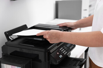 Woman using modern printer at workplace indoors, closeup