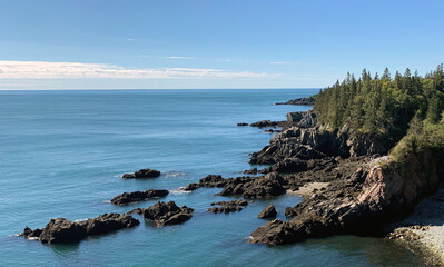 Rocky beach below coastal bluff set against a clear blue sky above east coast waters along the Butler Bold Coast Trail in Maine, USA. © Jason