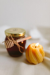 Organic honey in a glass jar and burning candles made of natural handmade wax on a white background. Beekeeping products. Small business. Farm.