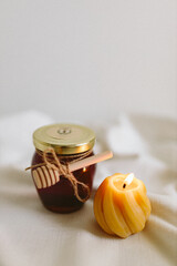 Organic honey in a glass jar and burning candles made of natural handmade wax on a white background. Beekeeping products. Small business. Farm.