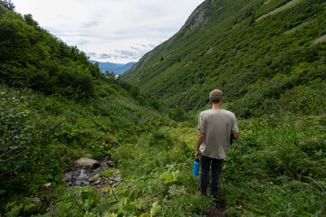 A solo hiker explores a lush, green mountain trail in Alaska’s Turnagain Arm region, surrounded by dense summer foliage and tranquil wilderness.