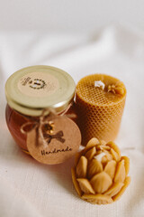 Organic honey in a glass jar and burning candles made of natural handmade wax on a white background. Beekeeping products. Small business. Farm.