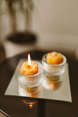 Burning candles made of natural handmade wax on a mirror tray in the dark in the house. Beekeeping products. Small business. Cozy interior with candles in the semi-darkness