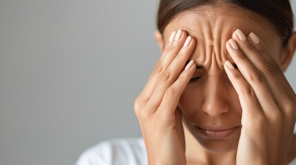 Fototapeta premium Close-up of a woman massaging her temples to relieve a headache, emphasizing stress relief and self-care techniques.