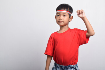 Cheerful Asian boy in red t-shirt raising his hand in air with happy and successful expression, isolated on white background. Indonesian Independence Day concept.