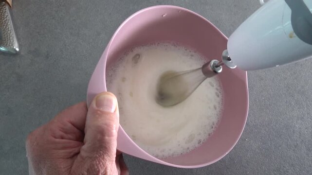 A cook whips egg whites with a hand mixer in a bowl. 