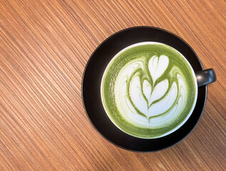 Top view photo, a black cup of hot matcha latte art, put on wooden table with warm light.