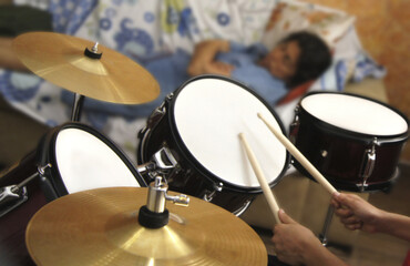 child's hands playing drums while blurred mom rests in the background lying on the sofa