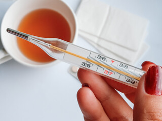 A thermometer in close-up against the background of a mug of tea and pills. The concept of ARI,...