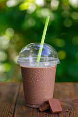 chocolate flavor milkshake or protein cocktail in disposable plastic glass with straw on wooden table