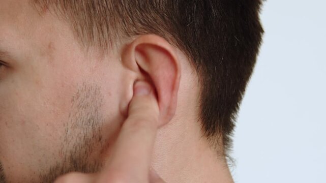 Caucasian man picking his left ear with his finger close up during plug in ear canal. Scratches and cleaning the ear canals for better hearing and massage of the ears. Insect gets into the ear.