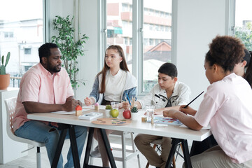 African American teacher man sitting on chair and teaching drawing and painting with watercolor of art for student or pupils in classroom at school. Education for artist Concept