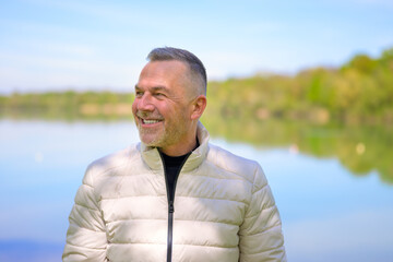 Smiling Older Man in a Light Jacket by the Lake looking to the left