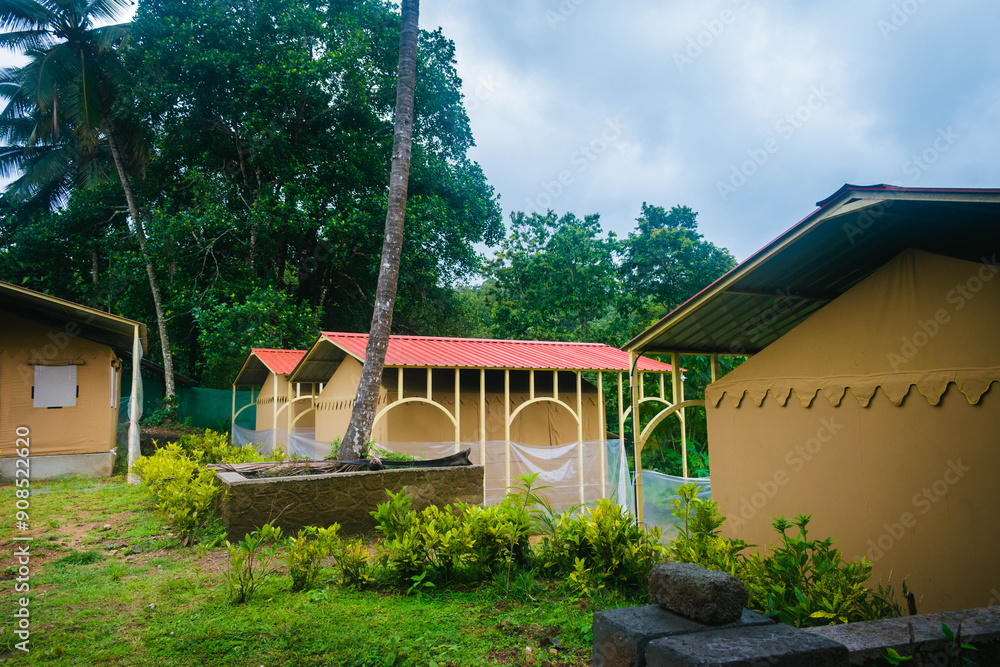 Wall mural tent-style structures with red roofs surrounded by plants and trees on an overcast day.