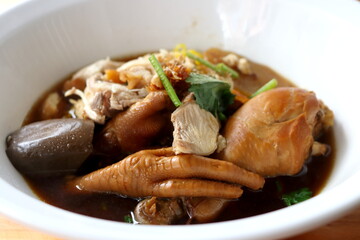 Close up beside view of braised drumstick and foot chicken Thai style soup egg noodle in white bowl in Thailand.