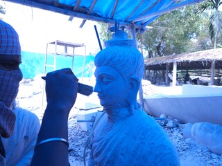 Artisan meticulously sculpting a detailed Red Stone Buddha Statue Using Precision Stone Carving...