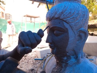 Artisan meticulously sculpting a detailed Red Stone Buddha Statue Using Precision Stone Carving...