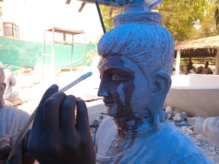 Artisan meticulously sculpting a detailed Red Stone Buddha Statue Using Precision Stone Carving...
