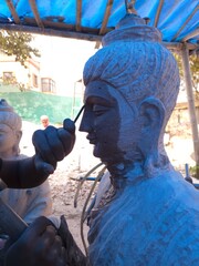 Artisan meticulously sculpting a detailed Red Stone Buddha Statue Using Precision Stone Carving...