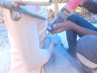 Artisan meticulously sculpting a detailed Red Stone Buddha Statue Using Precision Stone Carving Compass In Odisha, India, tools in hand.