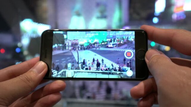 A person is holding a cell phone and looking at a video of a bus. The video is playing on the phone's screen