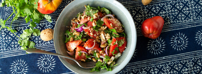 bowl with salad of tomatoes, red onions and walnuts on the table, top view