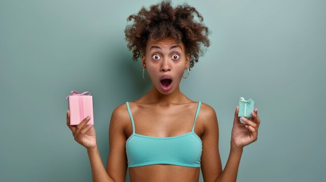 Surprised woman in a green bra holding two different gift boxes, standing against a green background.